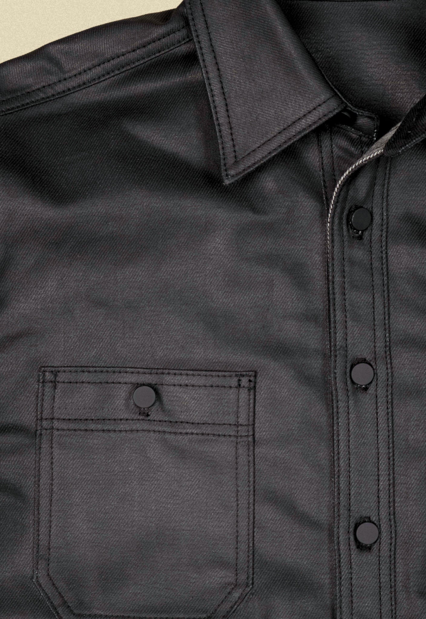 Close up of a black denim button-up chore shacket on a beige background