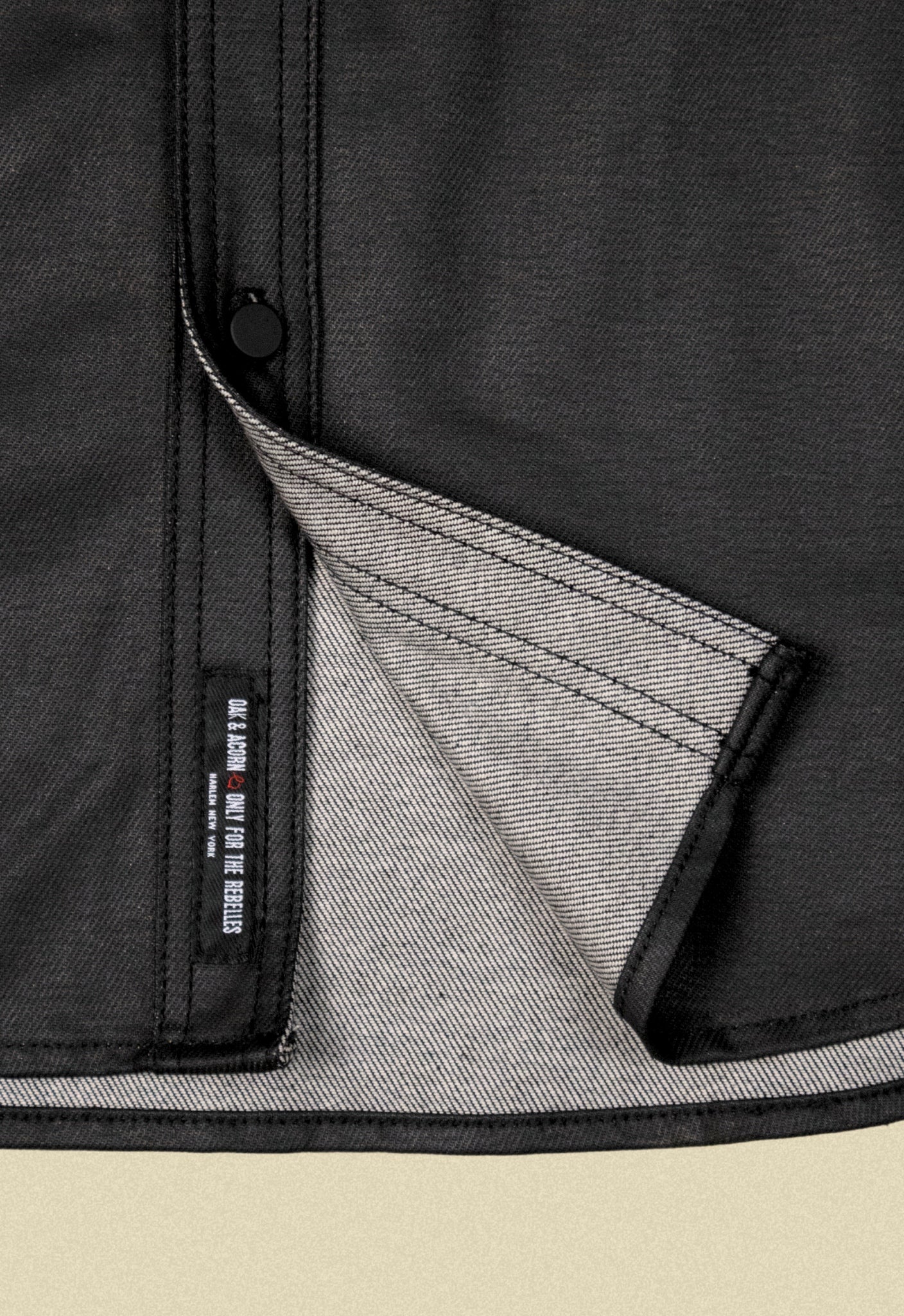 Close up of a black denim button-up chore shacket on a beige background