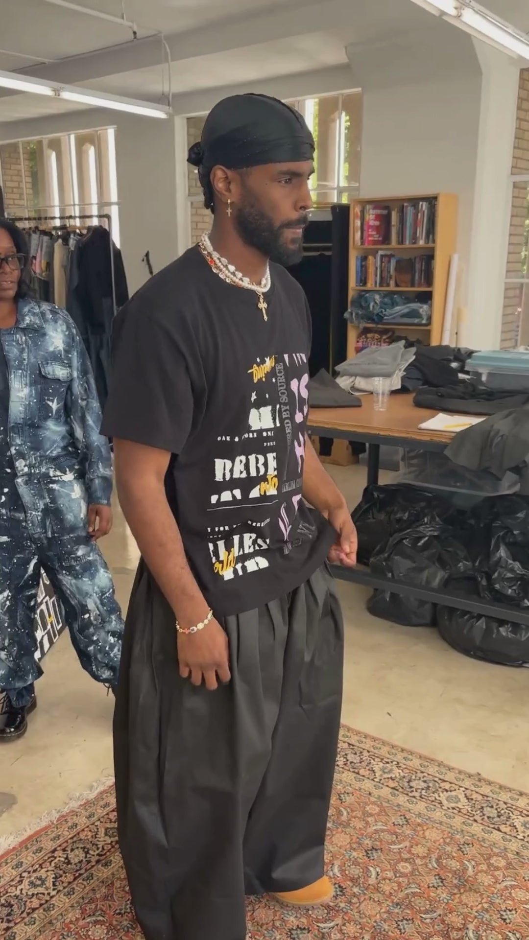 Man wearing coated black denim double waistband wide-leg trousers and black t-shirt in an apparel design studio atelier.